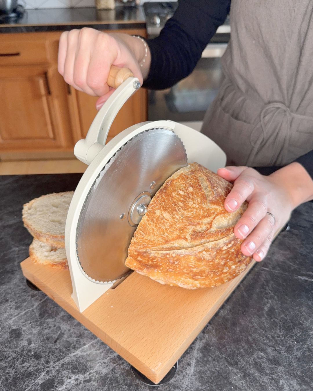 Person using a manual bread slicer to cut a loaf of bread on a kitchen counter.