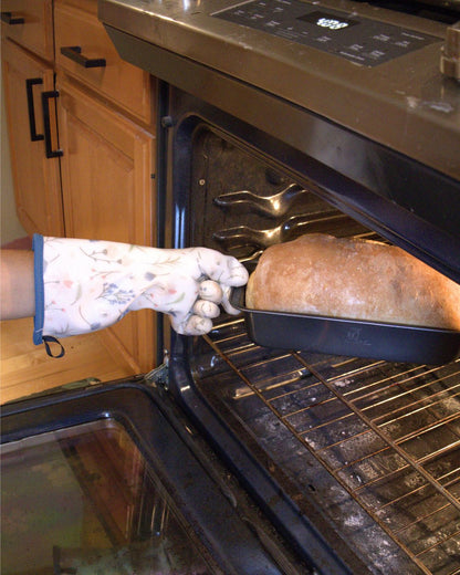A gloved hand reaching into the oven to lift out a finished loaf